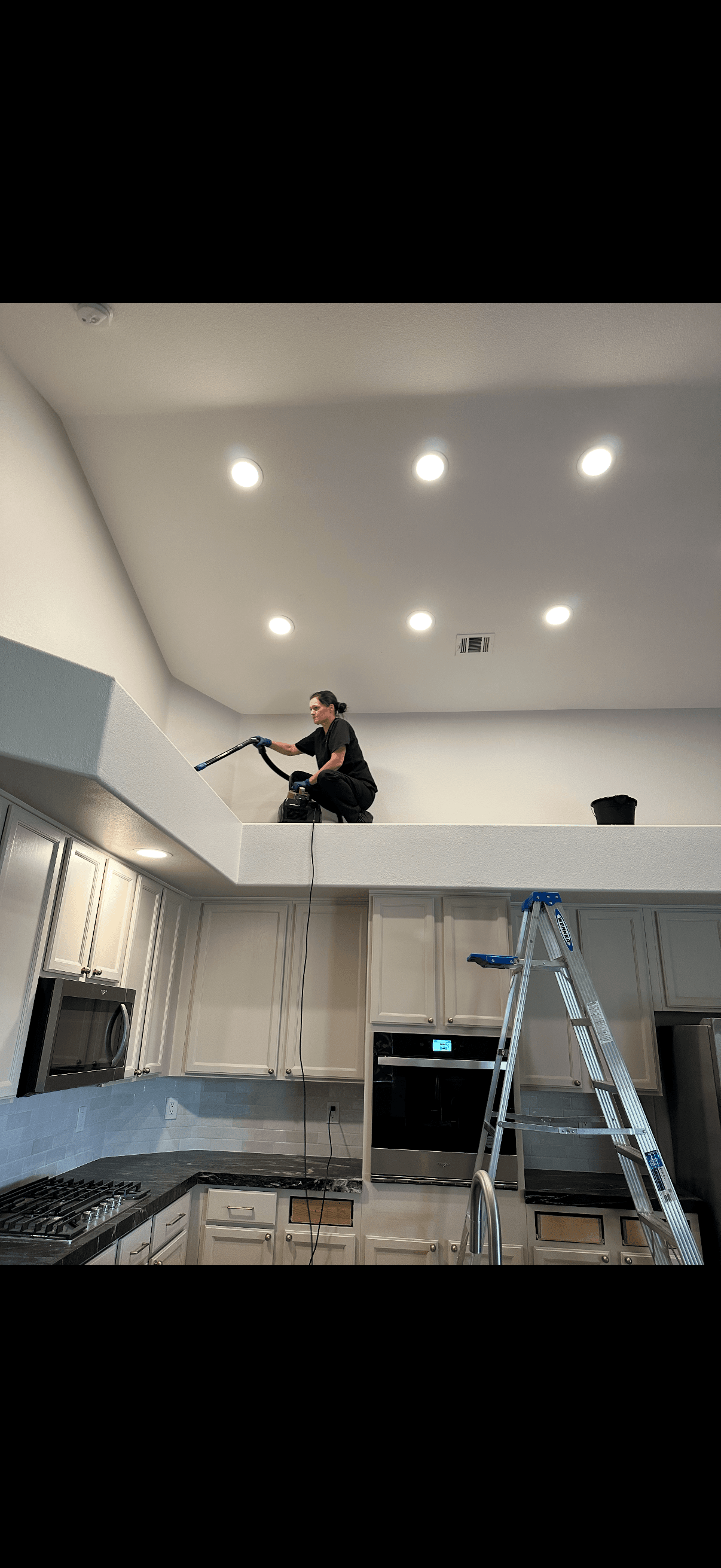 Vital Cleaning team member vacuuming a high ledge above kitchen cabinets